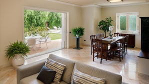 A spacious living area with a sofa, dining table, and chairs. There is a sliding glass door leading to an outdoor patio with a garden view. - Villa Lia (Sant'Agnello)