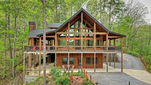 A two-story log cabin with a balcony, surrounded by a forest.