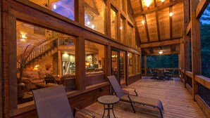 A spacious wooden deck with a cozy seating area, a staircase leading to an upper level, and large windows offering views of the outdoors.