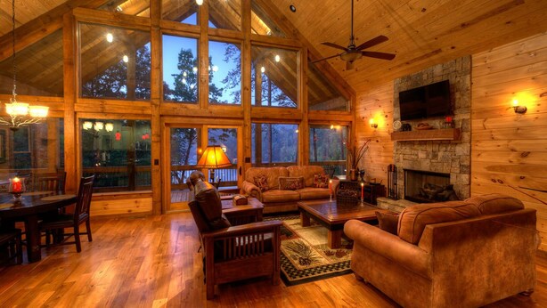 A spacious living room with a high ceiling, large windows, a fireplace, and a cozy seating area.