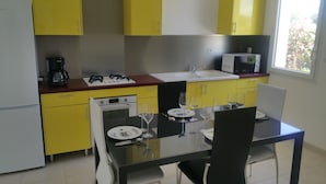 A compact kitchen with yellow cabinets, a microwave, a stove, and a dining table set for two with wine glasses. - House of 50 m2 living space with large landscaped garden (Vineuil)