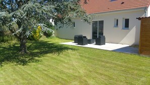 A modern house with a well-maintained lawn, outdoor seating area, and a large tree providing shade. - House of 50 m2 living space with large landscaped garden (Vineuil)