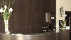 A reception desk with a dark wood finish and the initials "RH" on it. There is a vase with white flowers on the left side of the desk. - HRS Hotel Sabatino (Follonica)