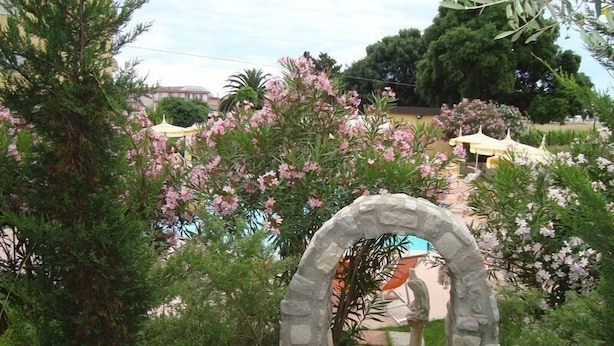 A stone archway leading to a pathway surrounded by lush greenery and flowering plants. - HRS Hotel Sabatino (Follonica)