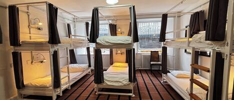 A dormitory-style room with bunk beds, a radiator, a chair, and a window with curtains.