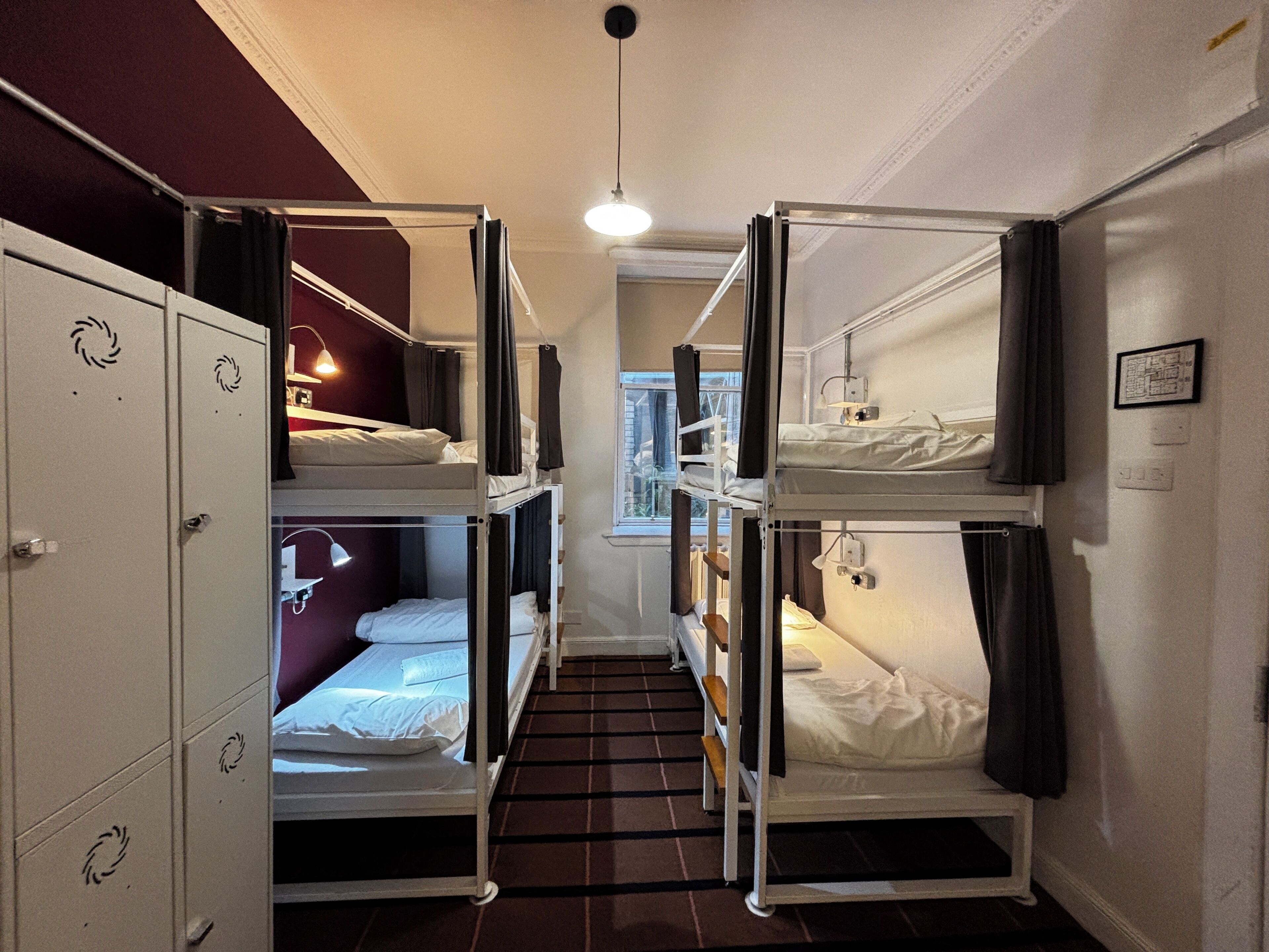 Ein Schlafsaalzimmer mit Etagenbetten, einem Kleiderschrank und einem Fenster mit Vorhängen.