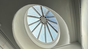 Una imponente escalera con barandilla blanca y un tragaluz circular en la parte superior. Un letrero indica las habitaciones 306-307.