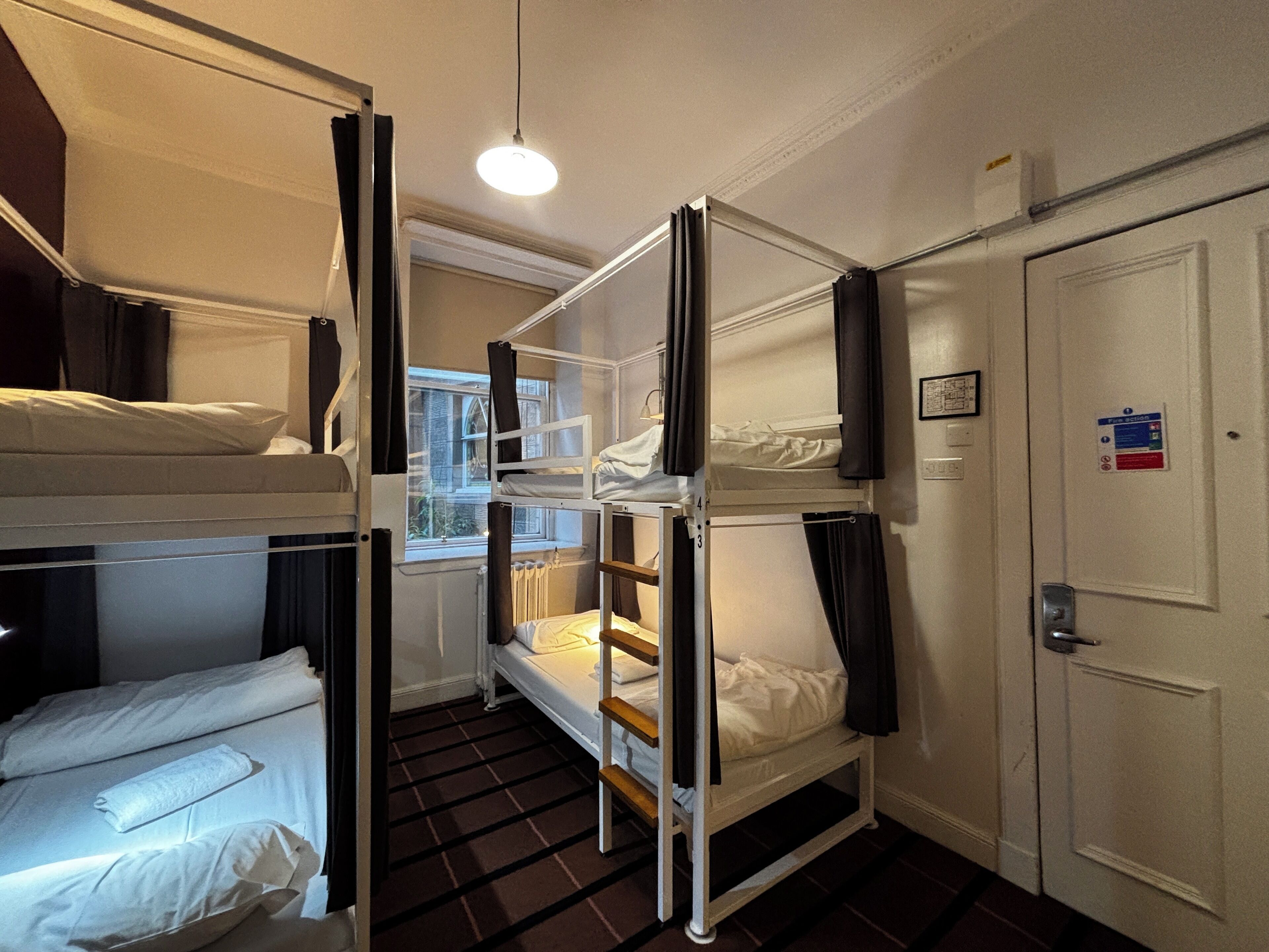 A room with bunk beds, a window, a door, and a light fixture.