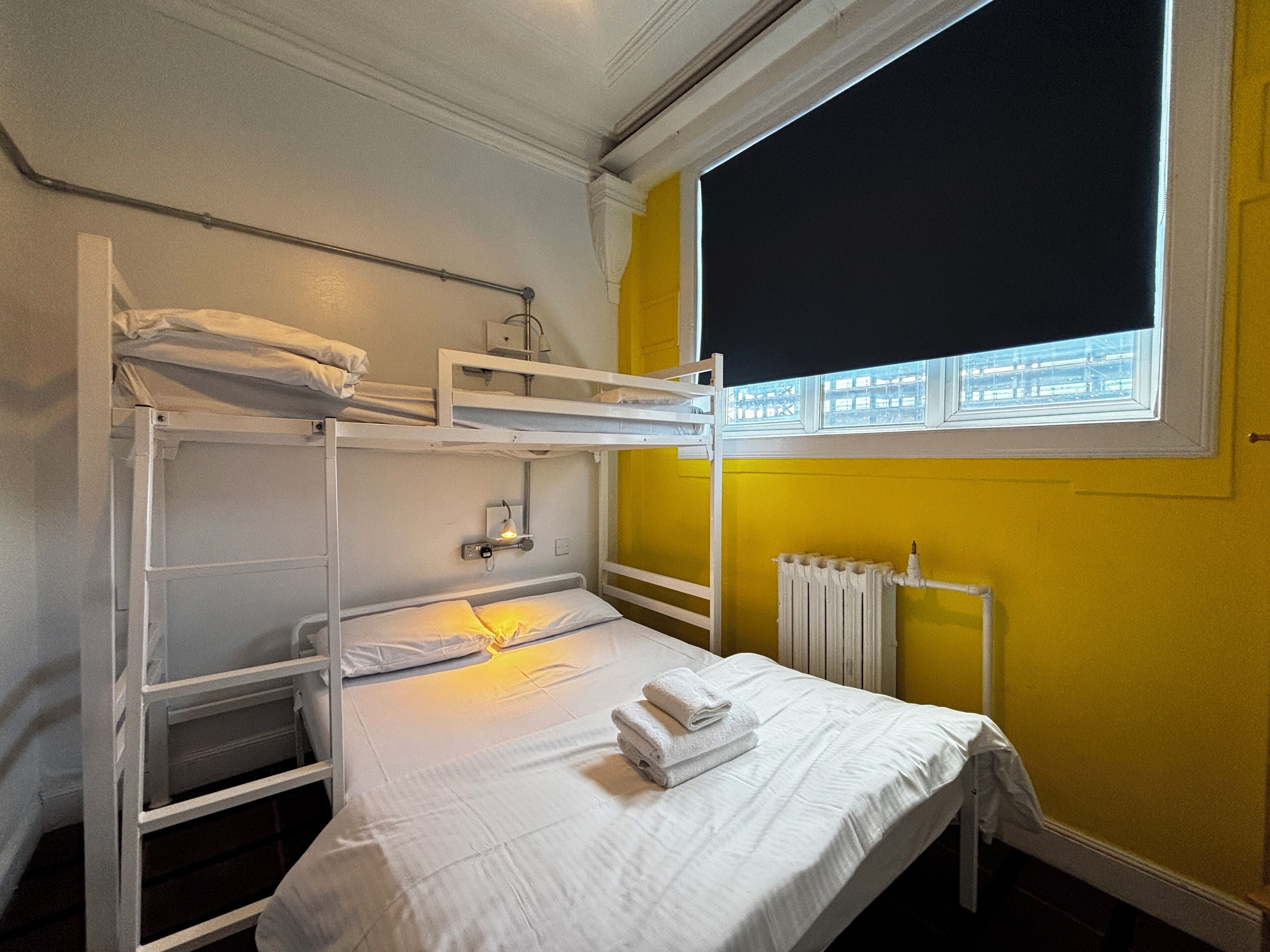 Ein Schlafraum mit Etagenbett, Fenster und weißer Bettdecke.