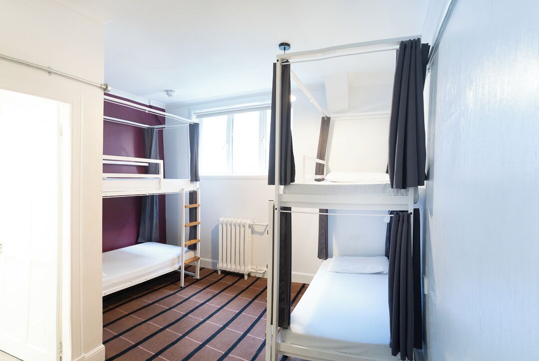 A bunk bed room with a window, a radiator, and a door.