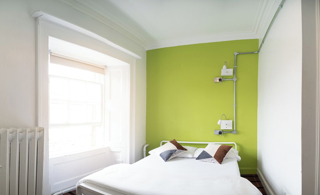 A room with a bed, a window, a radiator, and a green wall.