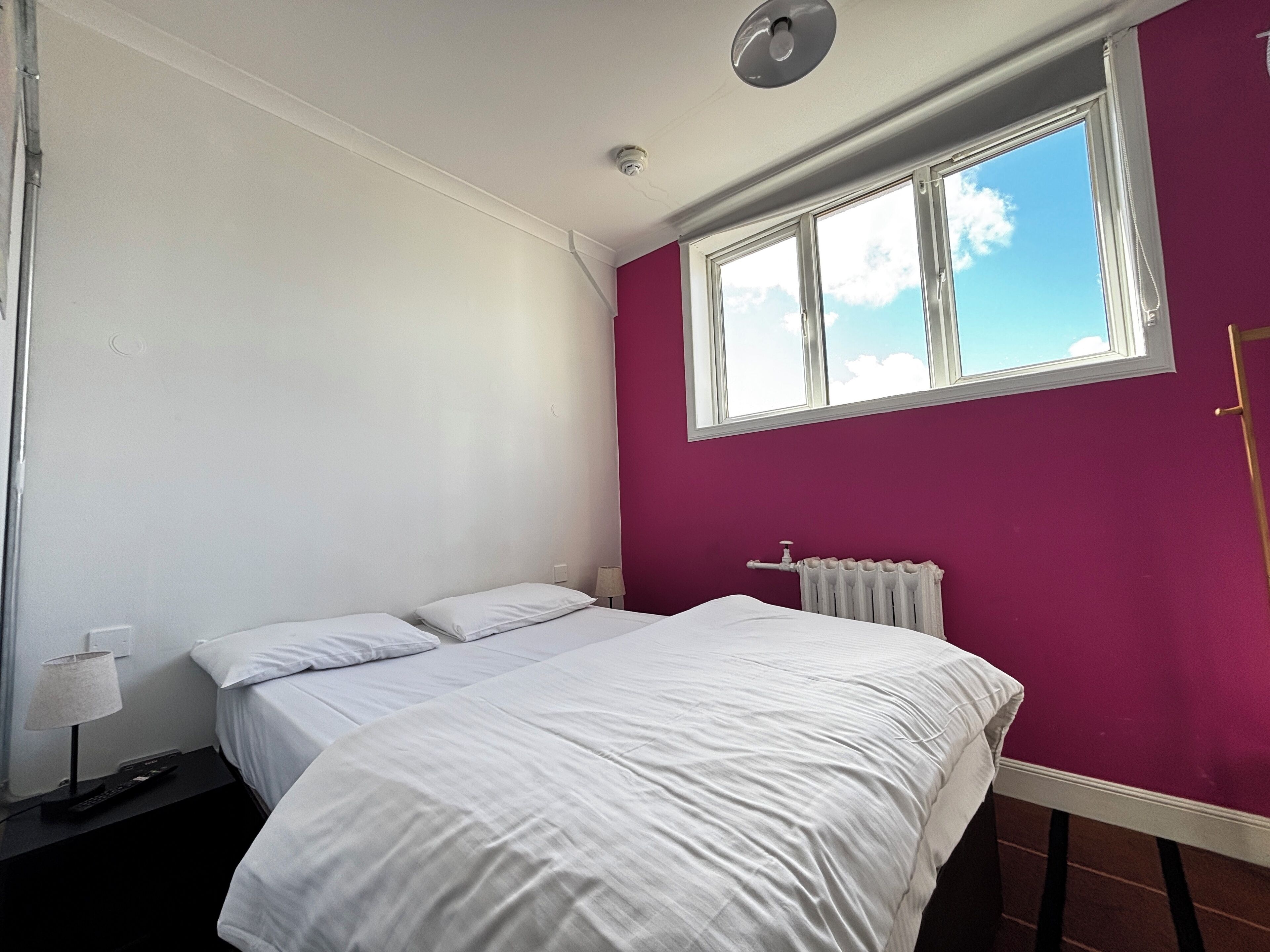Een slaapkamer met een bed, een raam, een radiator en een lamp.