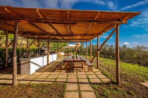 Un patio exterior con mesa y bancos de madera, rodeado por una pérgola.