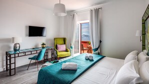A hotel room with a bed, a desk with a chair, a television, and a view of the outdoors. - Casa Aprea (Massa Lubrense)