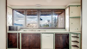 A kitchen with a large window, wooden cabinets, a microwave, and a dishwasher. - Casa Aprea (Massa Lubrense)