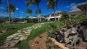 A well-maintained garden with a stone pathway, palm trees, and a modern house with a large deck. - Villa MAISON BLANC BLEU – Iconic Elegance Above Gouverneur (Gustavia)