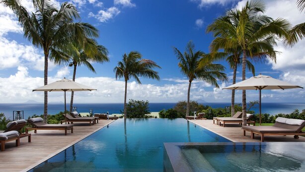 A pool area with lounge chairs and umbrellas, surrounded by palm trees and overlooking the ocean. - Villa MAISON BLANC BLEU – Iconic Elegance Above Gouverneur (Gustavia)