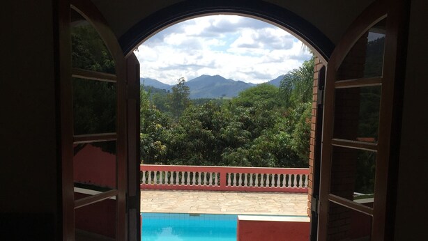 An open doorway leading to a pool area with a view of mountains and greenery. - A Dream in the Mantiqueira Mountains (Itamonte)