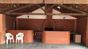 An outdoor kitchen area with brick walls, a tiled floor, and two white plastic chairs. - A Dream in the Mantiqueira Mountains (Itamonte)