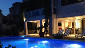 A swimming pool with a clear blue water surface, surrounded by lounge chairs and potted plants.