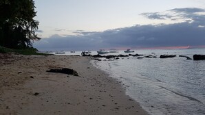 Une plage avec des bateaux, des rochers et un coucher de soleil.