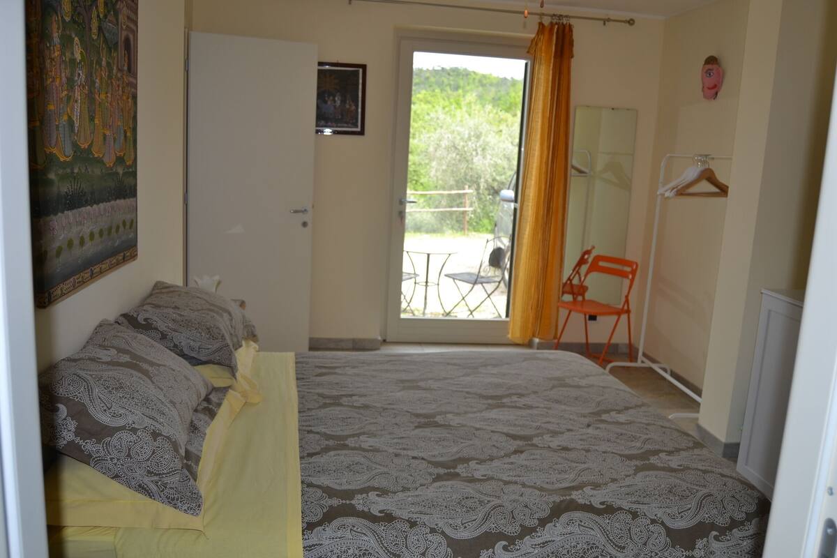 Un dormitorio con cama, una silla, una puerta y un balcón con mesa y sillas.
