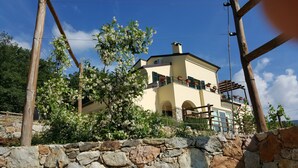 Un bâtiment à deux étages, avec un mur de pierre à l’avant, un balcon orné de plantes en pot et un ciel d’un bleu éclatant.