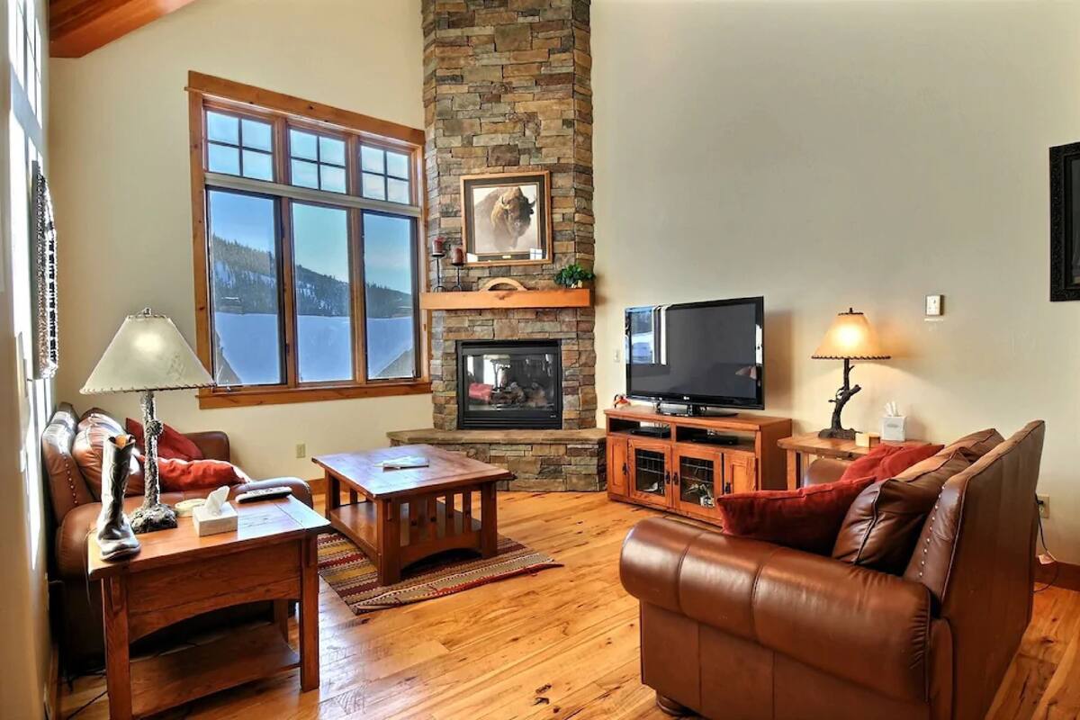 A cozy living room with a stone fireplace, leather sofa, wooden coffee table, and a television.