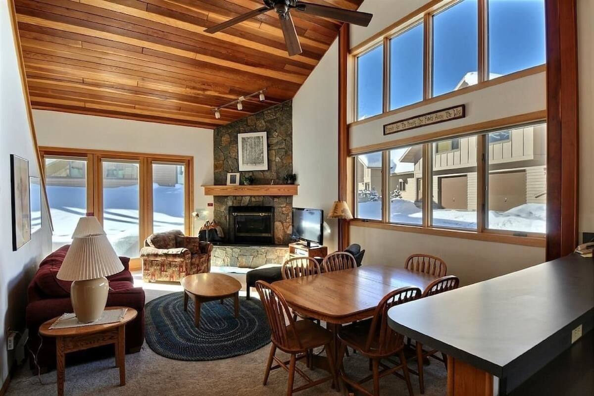 A cozy living room with a fireplace, wooden ceiling, and large windows overlooking a snowy landscape.