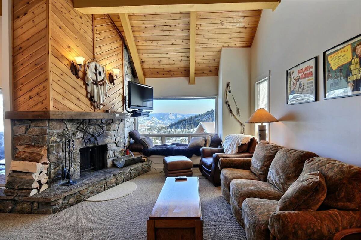 A cozy living room with a stone fireplace, wooden ceiling beams, and a view of the mountains.