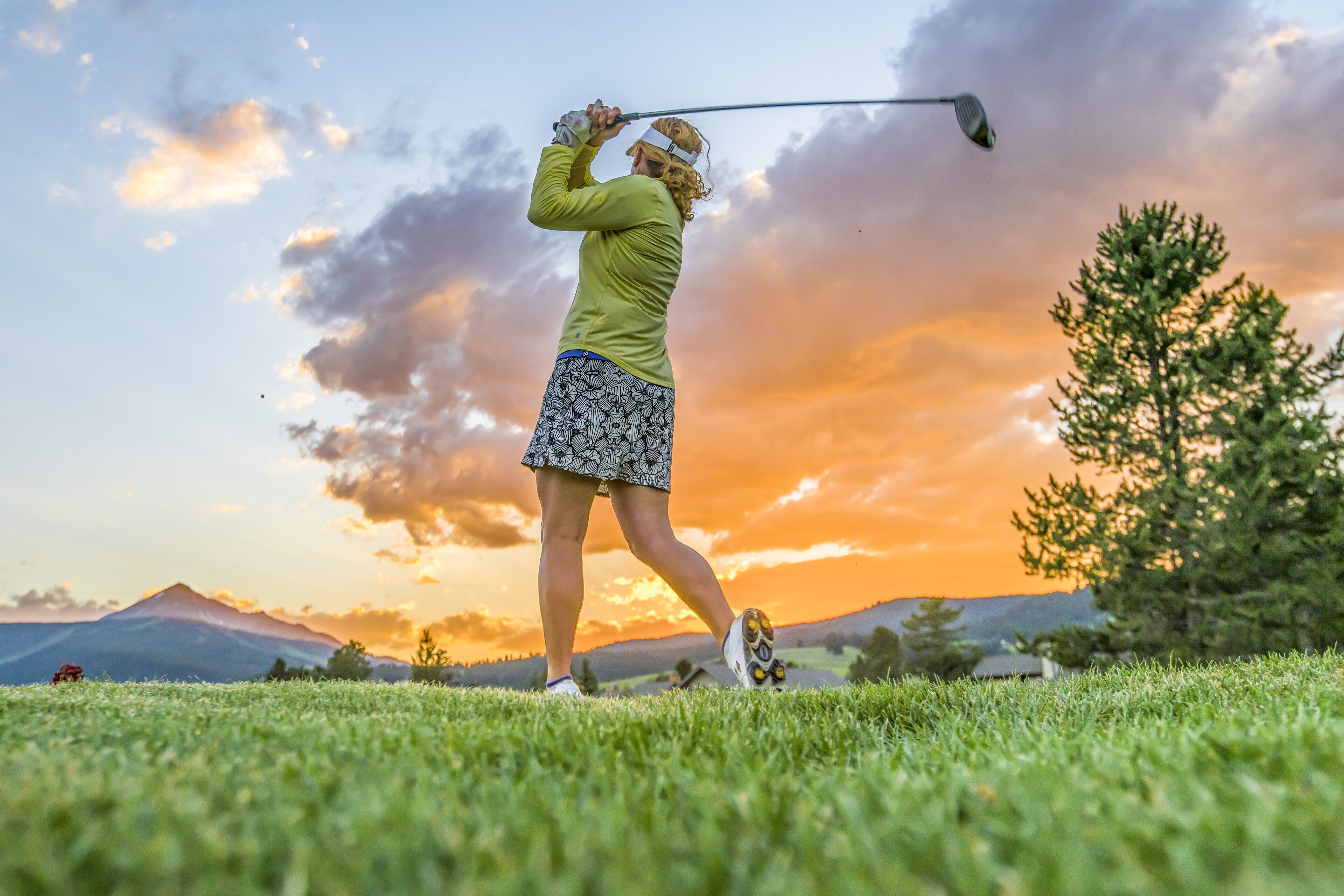Una persona juega al golf en un campo cubierto de hierba, con un atardecer de fondo.