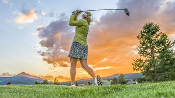 Una persona juega al golf en un campo cubierto de hierba, con un atardecer de fondo.