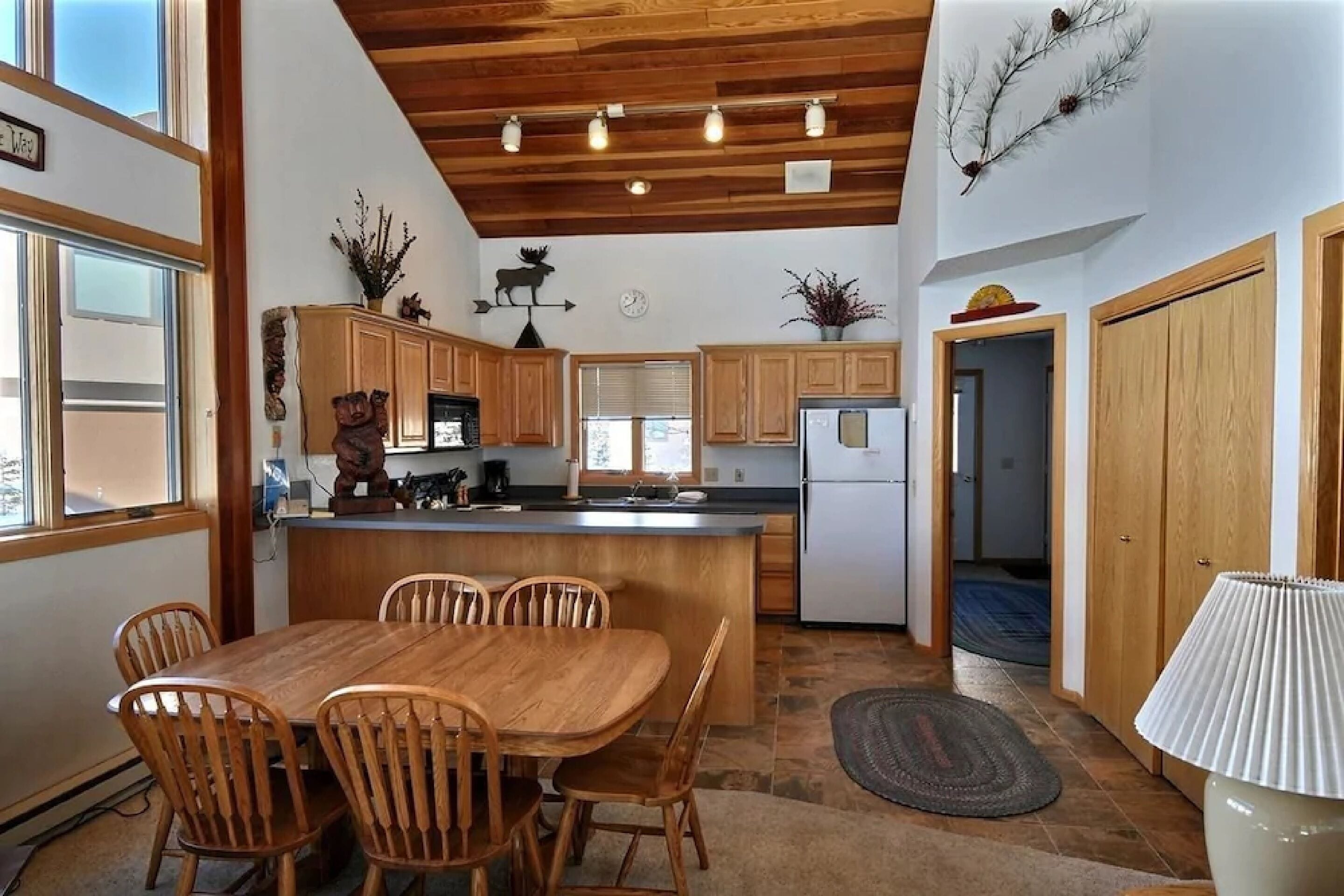 A kitchen with wooden cabinets, a central island with chairs, a refrigerator, and a dining table.