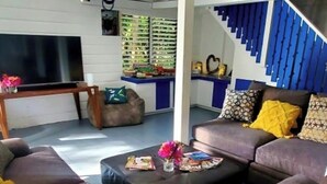A living room with a sofa set, a coffee table with magazines, and a TV. - Bak A Yaad Timberland Cottage (Negril)