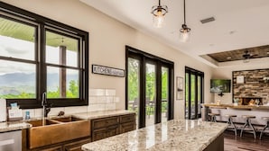 A modern kitchen with a large island, dark wood cabinets, and a view of mountains through large windows.
