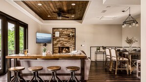 A modern kitchen with a stone backsplash, wooden bar stools, and a dining area with a rustic wooden table and chairs.