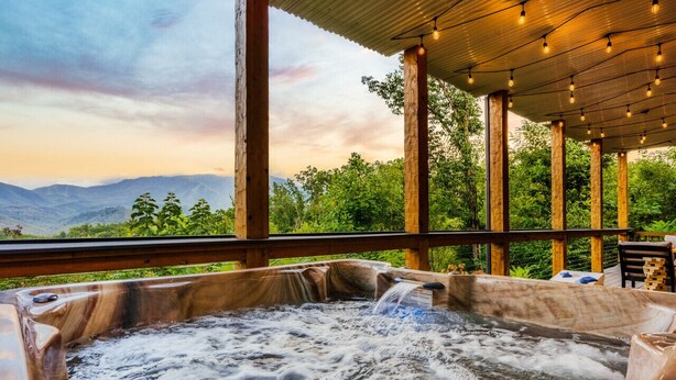 A hot tub with a waterfall feature, surrounded by wooden pillars and a covered area with hanging lights.