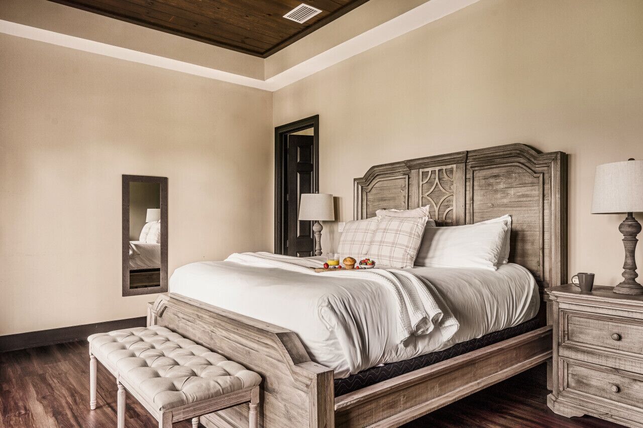 A bedroom with a large bed, a nightstand, a bench, and a mirror.