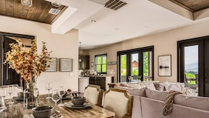 A spacious dining area with a wooden table set for six, a sofa, and a view of the kitchen and outdoors.
