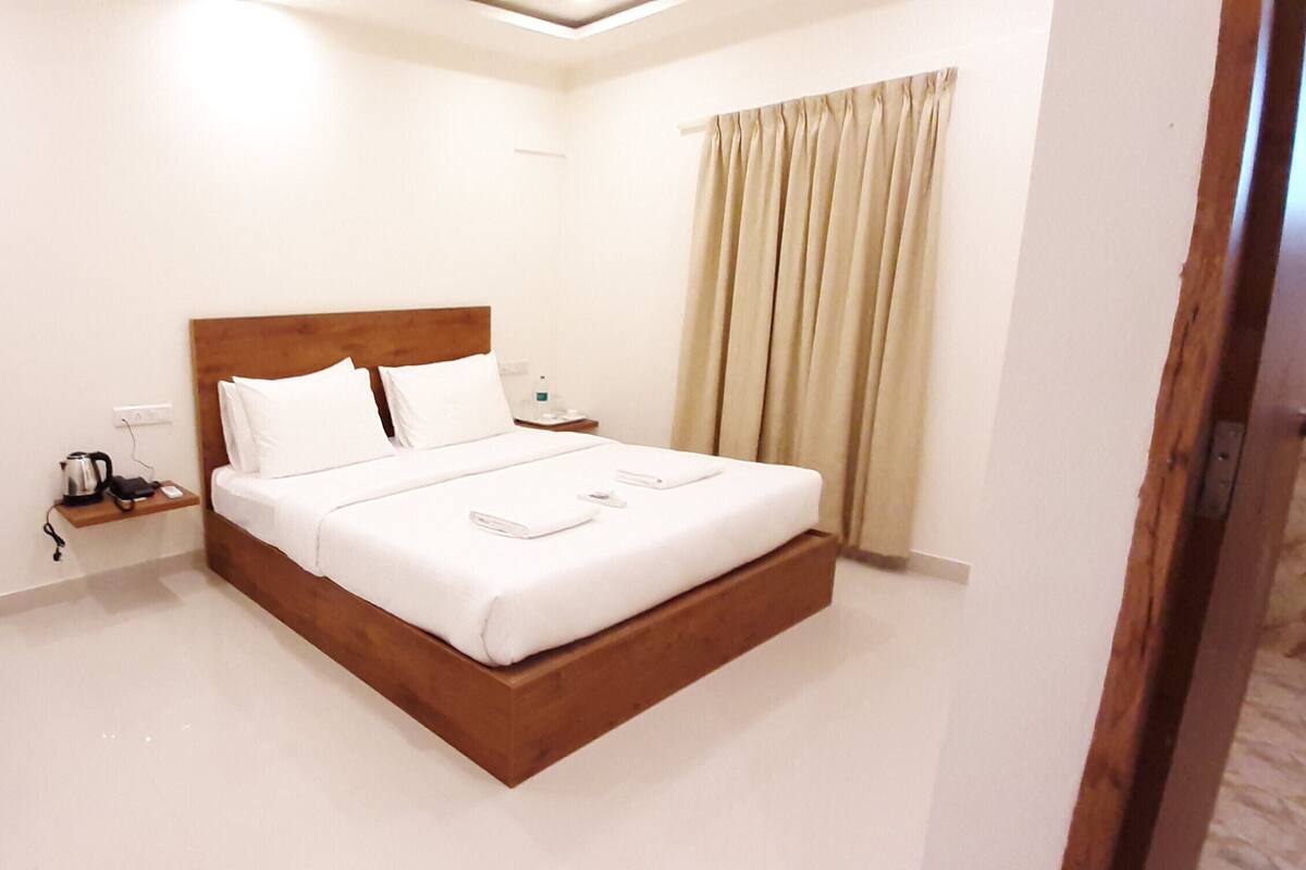 Habitación de hotel con una cama individual, mesita de noche y cortinas en la ventana. También hay dos sillones.