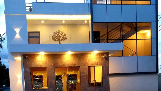 A modern hotel building with a prominent sign, a tree mural, and a well-lit entrance.