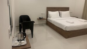 A neatly arranged hotel room with a bed, a chair, a bedside table with a phone, and a tray with a coffee maker, cups, and spoons.