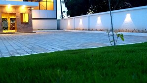 A modern building with a paved courtyard, illuminated entrance, and a well-maintained lawn.
