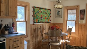 Ein gemütliches Blockhaus-Interieur mit Holzwänden, einem Essbereich mit Tisch und Stühlen, einer Küche mit Holzschränken und einem großen Fenster.