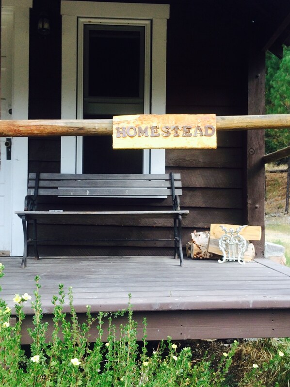 A wooden bench with a sign that reads "HOMESTEAD" on a porch. - Owner’s Favorite - A Quaint Historic Cabin in the Heart of the Swan Valley (Condon)