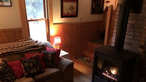 Ein gemütliches Wohnzimmer mit Kamin, einer Couch mit gemusterten Kissen, einer Lampe und einem gerahmten Bild an der Wand.