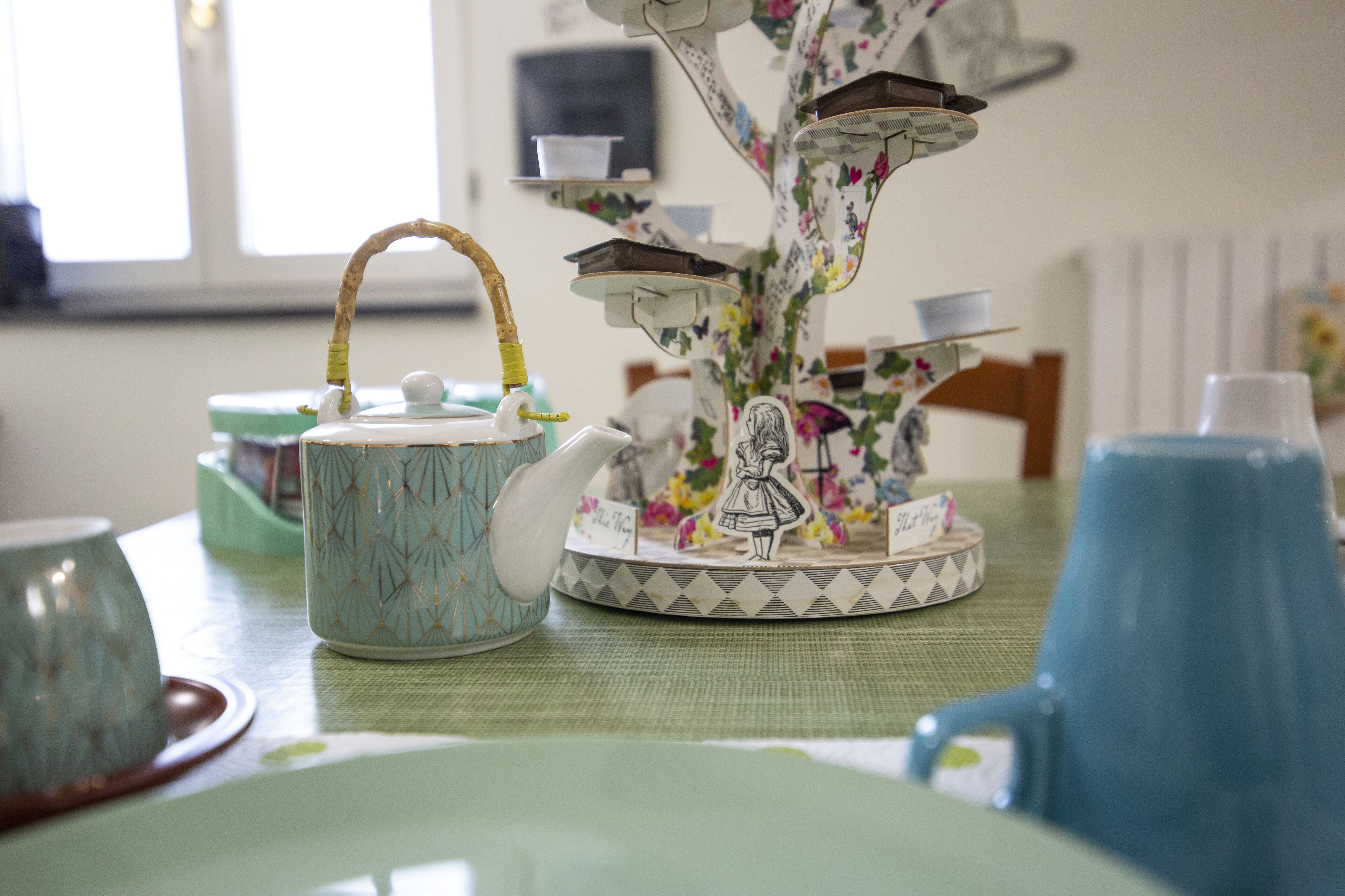 Una mesa con una tetera de estampado floral, una taza de cerámica y un jarro azul.