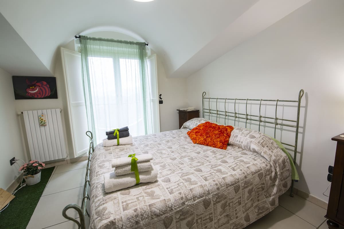 A bedroom with a bed, a radiator, a window with curtains, and a green plant.
