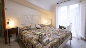 A neatly made bed with a patterned bedspread, two bedside tables with lamps, and a window with sheer curtains. - B&B Delle Meraviglie (Pellezzano)