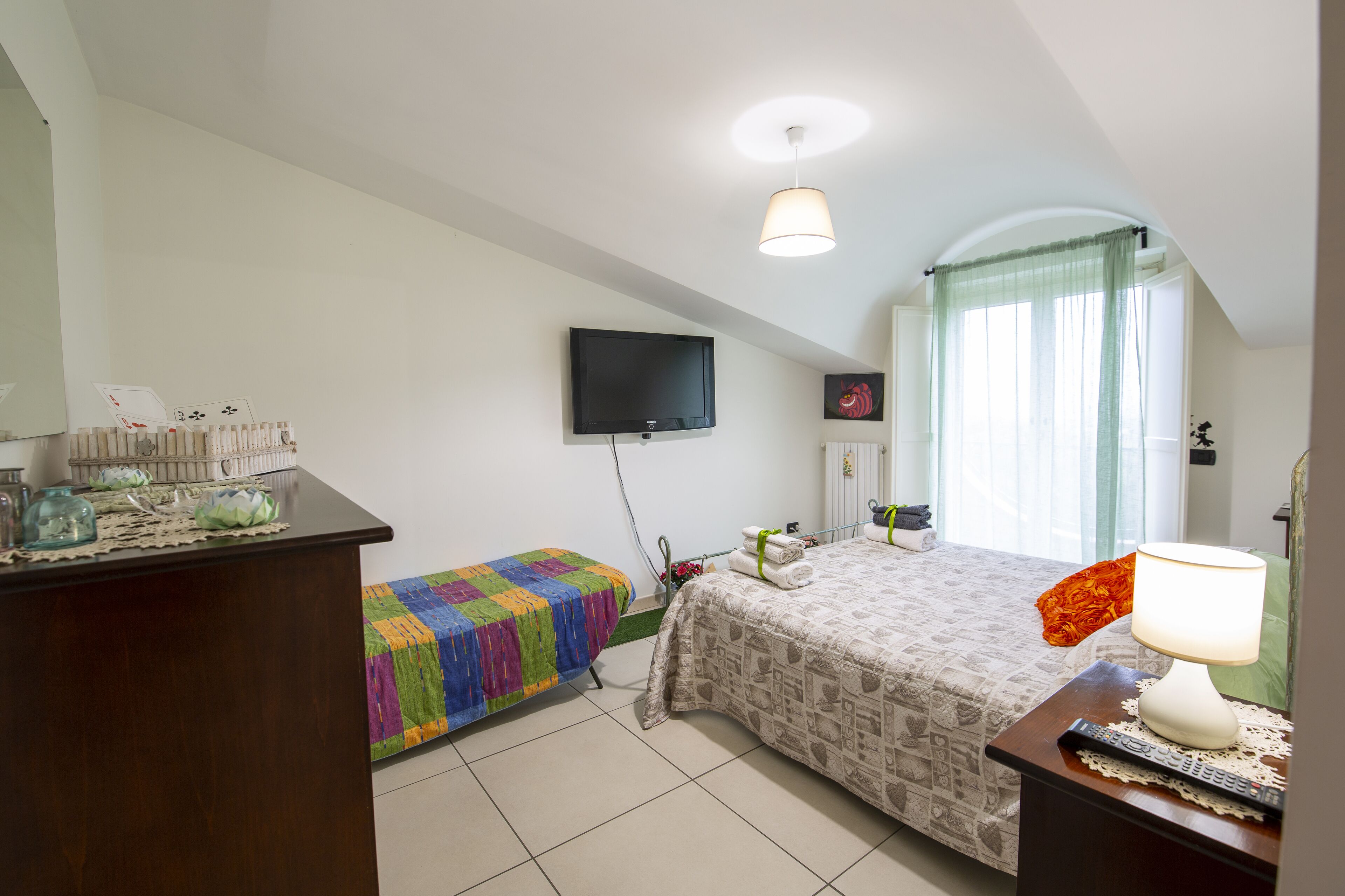 A bedroom with a bed, a desk, a television, and a window with curtains.